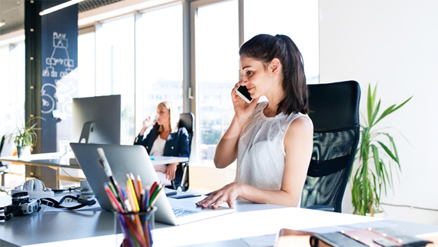 A female co worker talking on a mobile phone at her desk